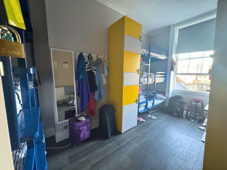 Interior of a shared room at Prime Backpackers Angel hostel in London, England, United Kingdom, featuring bunk beds, colorful lockers, dark floors, and a large window.