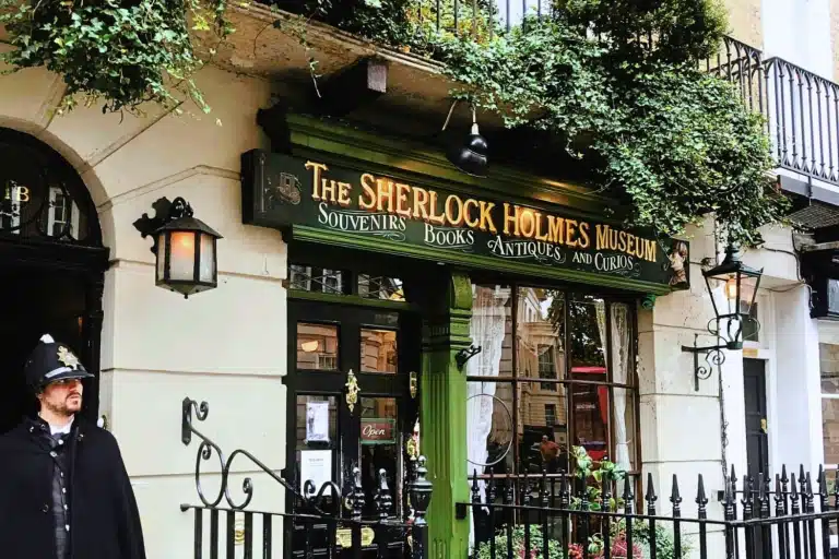 Exterior of the Sherlock Holmes Museum with green signage and a uniformed British bobby standing near the entrance at 221B Baker Street, surrounded by decorative period details in London, England, United Kingdom.