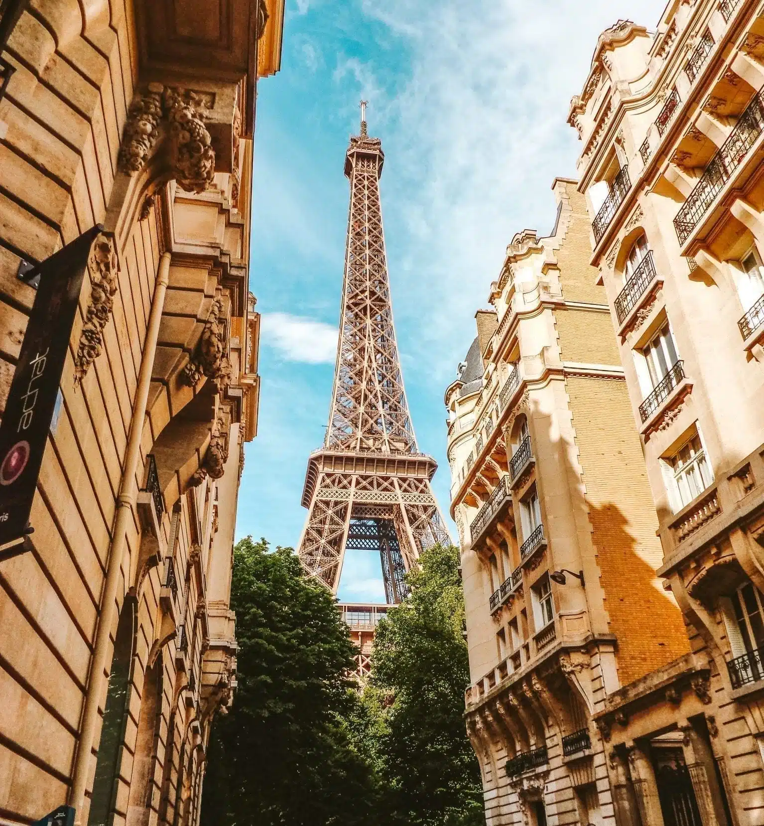 Home 30 View of the Eiffel Tower in Paris, France, from a side street framed by trees, Parisian buildings, and a blue sky.