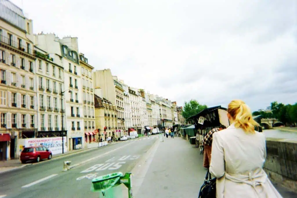 How to Spend a Day in Paris, France: An Affordable, Speedy Itinerary 34 The back of a blonde woman walking down a cobblestone street in Paris, France with classic Parisian architecture in the background. Captures a candid travel moment ideal for a Paris itinerary.