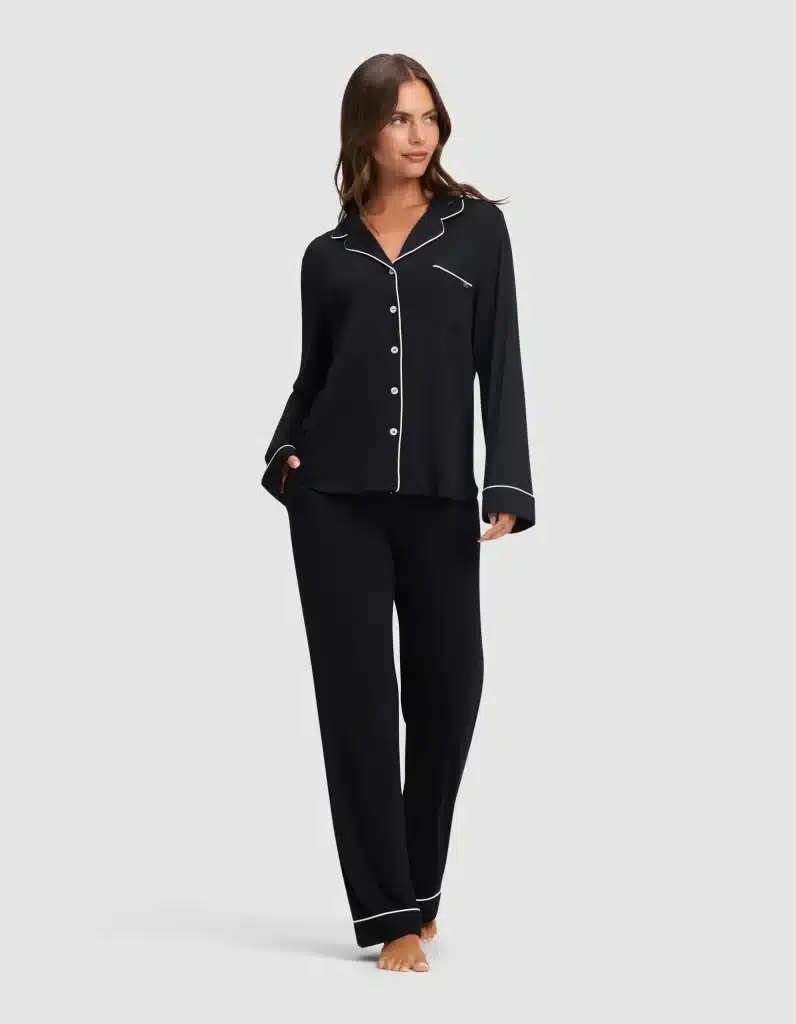 What to Wear in Greece: A Practical Packing List for Women 10 Woman with long brown hair models a black women's Cozy Earth bamboo stretch knit classic pajama pant set featuring a button-front long-sleeve top with notched collar, white contrast piping trim, chest pocket, and matching full-length wide-leg pants with white piped hem, against a light gray background.