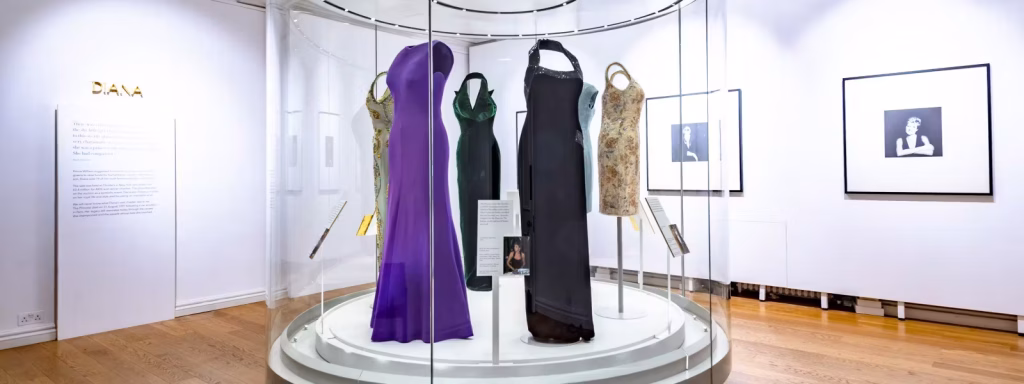 London 2-Day Itinerary: The Best Attractions for First-Timers + Downloadable Map 8 Several of Princess Diana's dresses on display at the Diana: Her Fashion Story Exhibit at Kensington Palace in London, England, United Kingdom, including a purple gown and a black sequined dress on a circular display with photos of Diana behind.