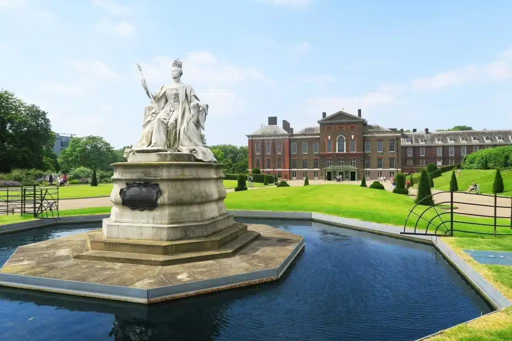London 2-Day Itinerary: The Best Attractions for First-Timers + Downloadable Map 7 Statue of Queen Victoria in a fountain in front of Kensington Palace, with the red-brick historic royal residence framed by green lawns and a clear blue sky in London, England, United Kingdom.