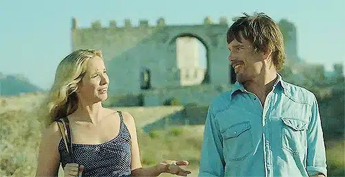 75 Movies Set in European Destinations to Inspire Your Next Trip 42 Animated GIF scene from Before Midnight showing Jesse and Céline walking and talking in the golden sunlight with a stone ruin in Greece behind them. Jesse wears a light denim shirt while Céline gestures mid-conversation in a sleeveless navy dress.