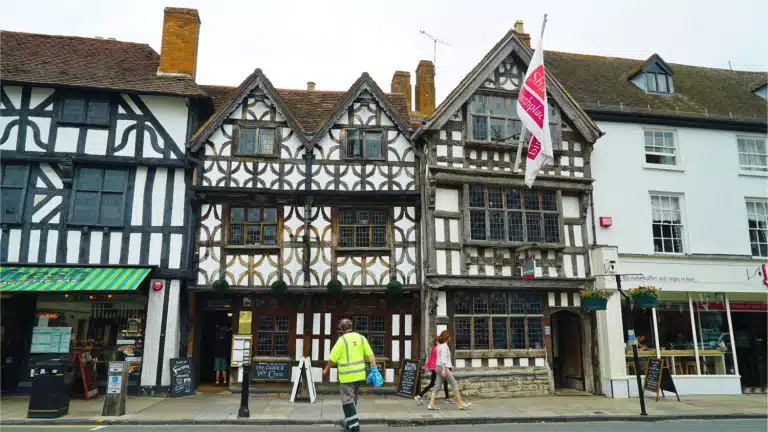 Is the Stratford Town Walk Worth It? A Review of the Guided Tour of Shakespeare's Hometown, Stratford-upon-Avon 18 Harvard House, a Tudor-style building with timber framing and a Shakespeare Birthplace Trust flag flying above the entrance, with visitors passing by on the street, in Stratford-upon-Avon, Warwickshire, England, United Kingdom.