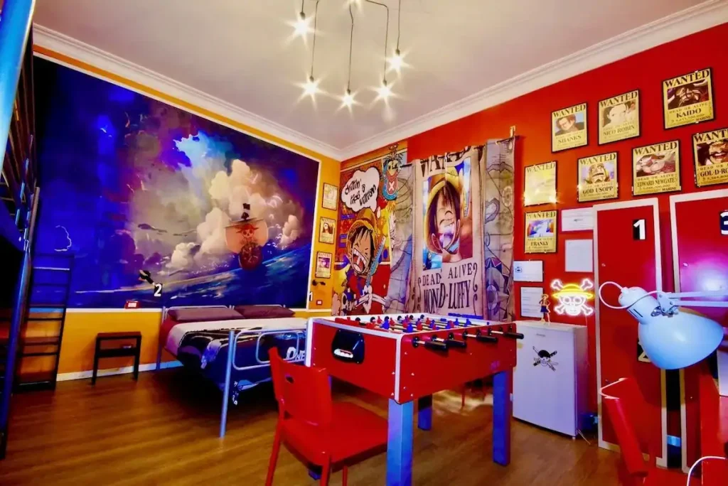 Reviewing Comics Guesthouse Roma as a Fan: Is It the Best Hostel in Rome, Italy? 5 One Piece–inspired room with character posters, a mural of the Thousand Sunny ship, and a foosball table, blending anime style with fun hostel amenities at Comics Guesthouse in Rome, Italy.