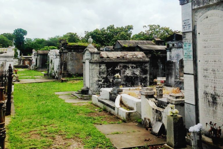 Lafayette Cemetery No. 1 in New Orleans, Louisiana, USA, seen on the Save Our Cemeteries tour of historic tombs and leafy trees casting dappled light across the grassy cemetery path.