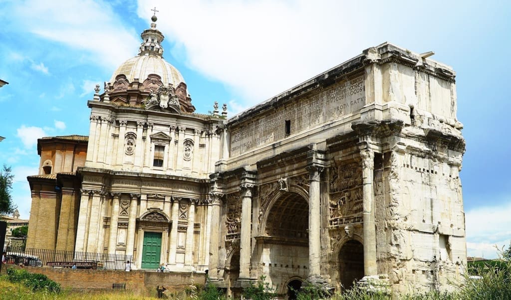 What It's Like to Visit the Roman Forum: A Visual Guide to Rome's Epic Ruins 28 Side view of the Arch of Septimius Severus at the Roman Forum in Rome, Italy, with detailed reliefs and Corinthian columns against a backdrop of ancient ruins.