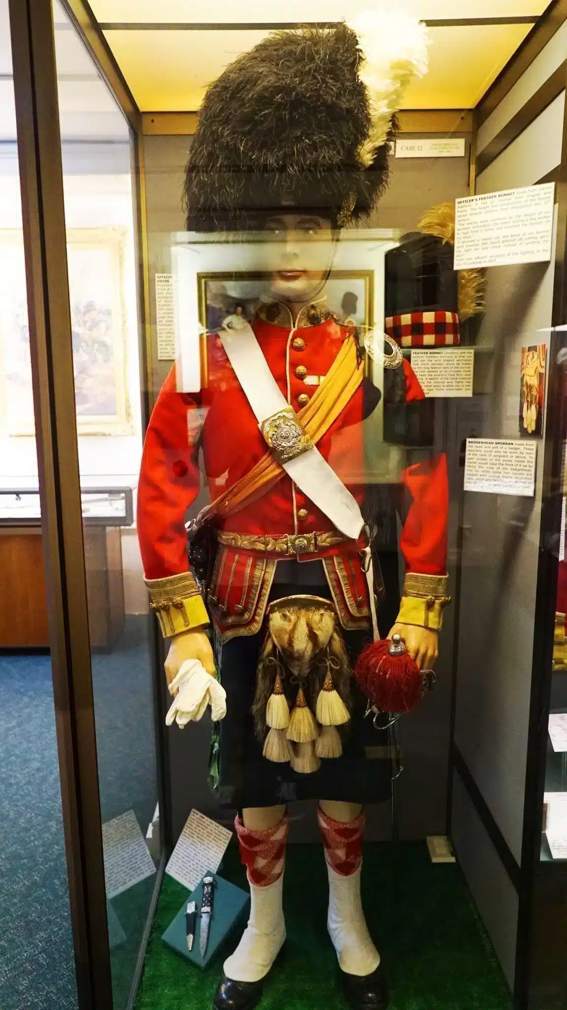 How to Visit Stirling Castle, Scotland: An Easy Day Trip by Train 30 Museum display case at Stirling Castle showing a mannequin in a Scottish Highland officer's dress uniform, including a red tunic with gold trim, dark kilt, badger-head sporran with tassels, white crossbelt, yellow sash, feather bonnet, and red and white hose.