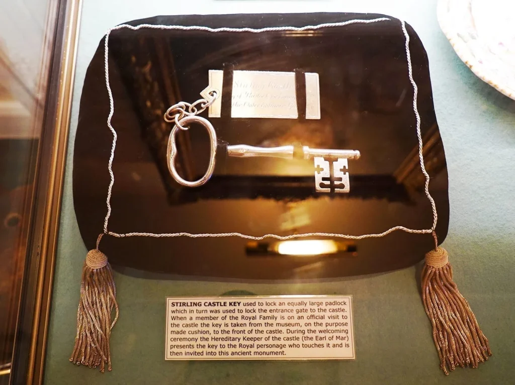 How to Visit Stirling Castle, Scotland: An Easy Day Trip by Train 32 Large castle key on display at Stirling Castle, mounted on a tasseled pillow with a label identifying it as part of the historical collection.