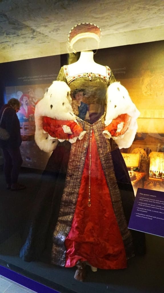 How to Visit Stirling Castle, Scotland: An Easy Day Trip by Train 18 A mannequin at Stirling Castle wearing a lavish Tudor‑style royal gown: deep green bodice with red brocade front panel, luxurious ermine‑trimmed fur sleeves, gold‑trimmed belt, and a matching red and gold headdress.
