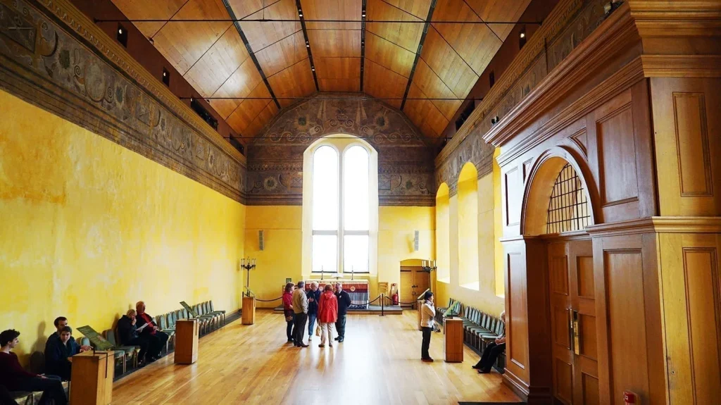 How to Visit Stirling Castle, Scotland: An Easy Day Trip by Train 5 Interior of the Old Chapel Royal at Stirling Castle, a historic building in Scotland, painted in a yellow color with frescoes lining the top section and a wooden ceiling, with tourists milling around the wooden floor.