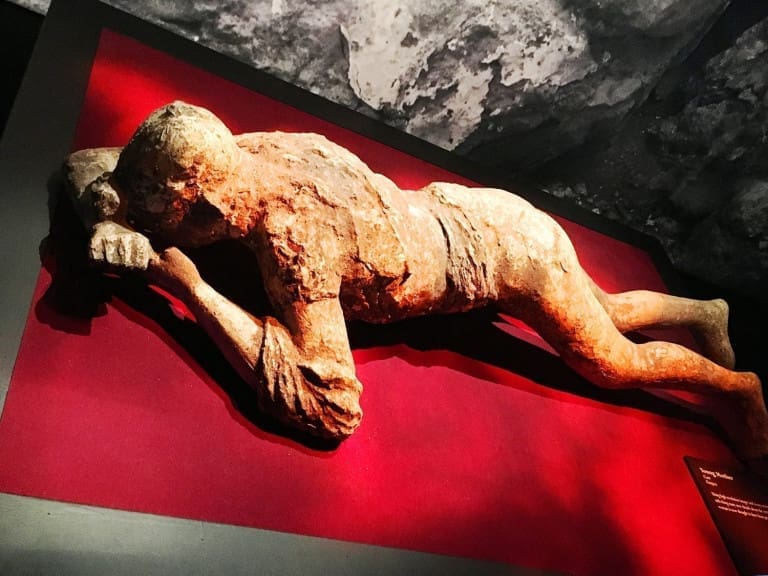 Plaster cast of a body from Pompeii on display at Pompeii: The Exhibition, showing a preserved figure lying face down with visible details of clothing and posture at the Ronald Reagan Presidential Library in Simi Valley, California, USA.
