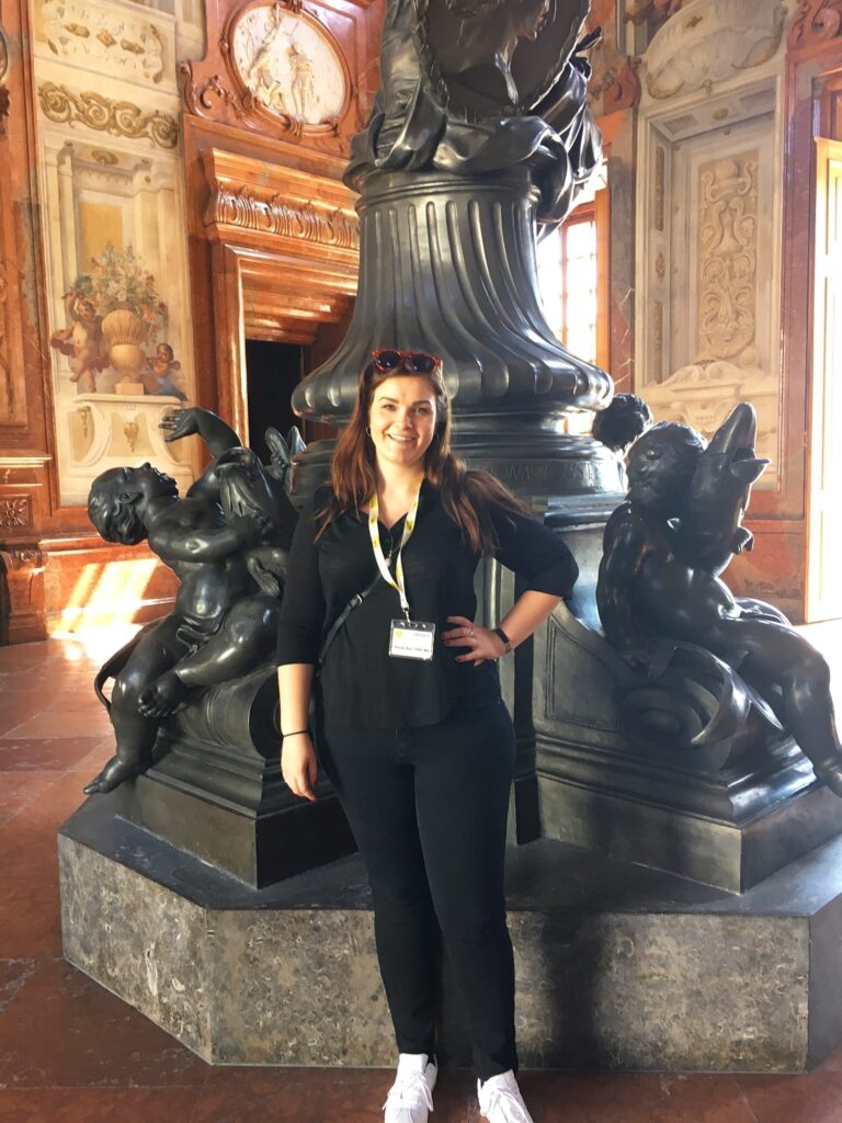 5-Day Austria Travel Itinerary: How to Visit Vienna and Salzburg on a Budget 32 Woman posing in the Lower Belvedere at Belvedere Palace in Vienna, standing in front of an ornate dark statue and decorative wall panels in a grand baroque interior.