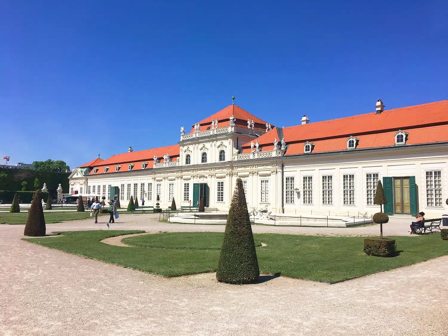 Exterior of the Upper Belvedere Palace in Vienna, Austria, featuring Baroque architecture with ornate detailing and green manicured hedges under a clear blue sky.