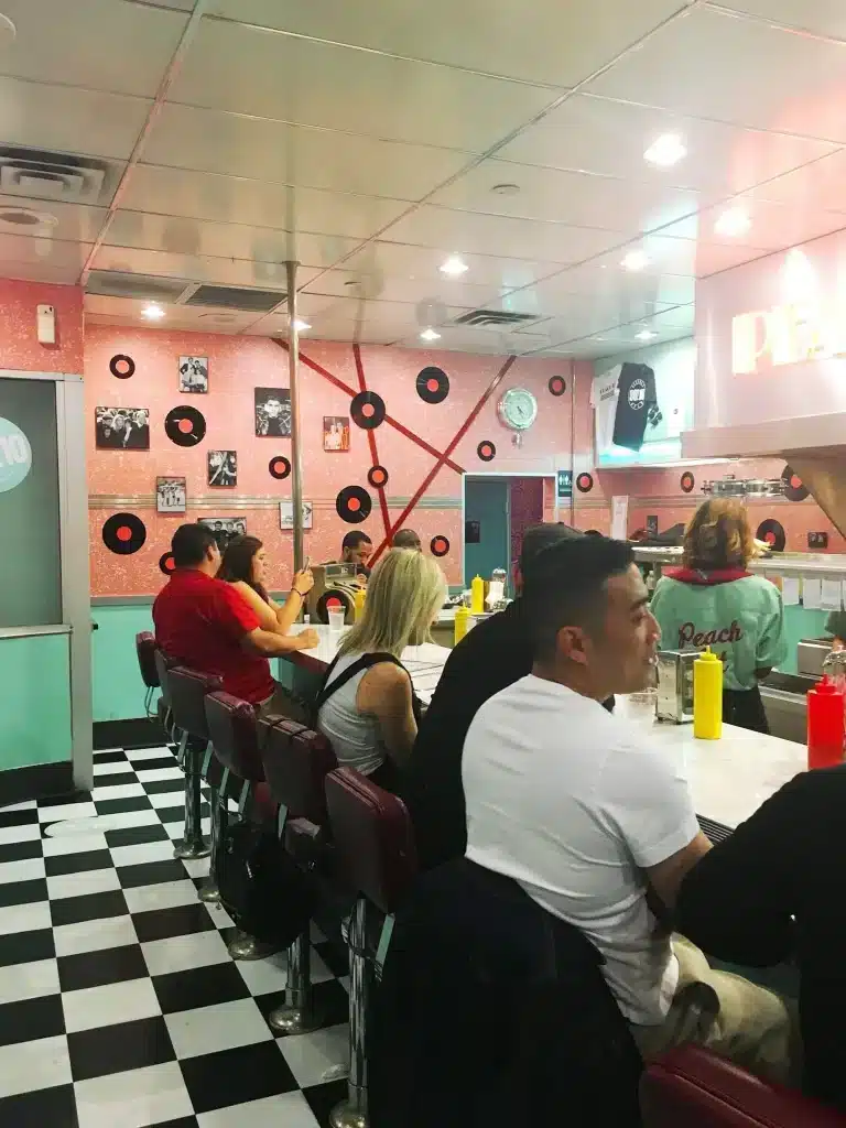 21 Cool, Nerdy Things to Do in LA—Activities for Kids to Adults 39 People sitting at the bar in a recreation of the Peach Pit Diner from 90210 in Los Angeles, set up as a themed pop-up experience.