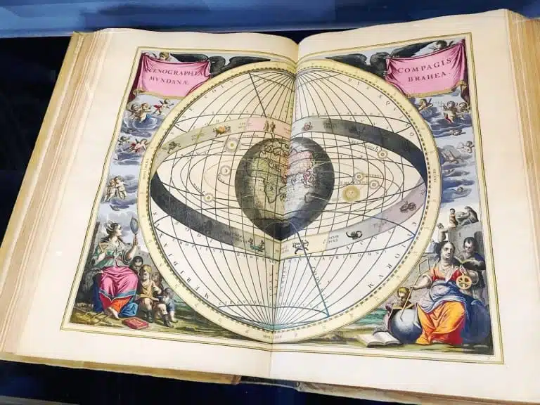 How to Visit The State Hall of the Austrian National Library in Vienna 16 A page from Andreas Cellarius’s celestial atlas Harmonia Macrocosmica on display at the Austrian National Library in Vienna, featuring colorful, detailed illustrations of astronomical constellations and planetary systems.
