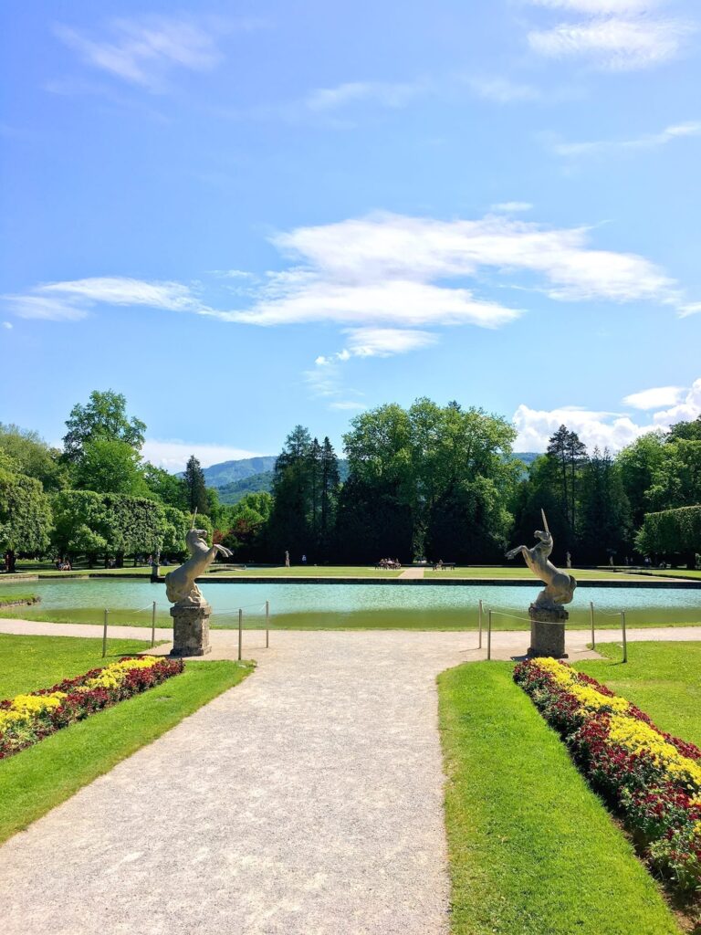 How Many Days in Salzburg, Austria? 1-, 2-, and 3-Day Itineraries 41 Beautifully manicured garden path leading to serene pond with statues and vibrant flowers at Schloss Hellbrunn Palace.