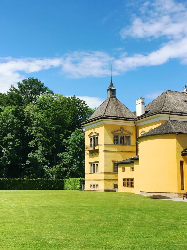 How Many Days in Salzburg, Austria? 1-, 2-, and 3-Day Itineraries 40 Historic Hellbrunn Palace with lush green lawn and forest backdrop under blue sky in Salzburg.