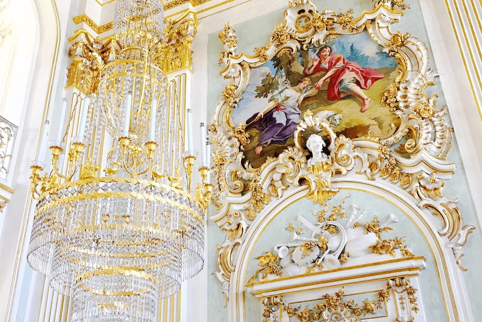 Germany 11 Ornate chandelier and artwork in the Great Hall at Nymphenburg Palace in Munich, Germany, featuring intricate gold detailing and a central fresco depicting classical figures surrounded by decorative molding.