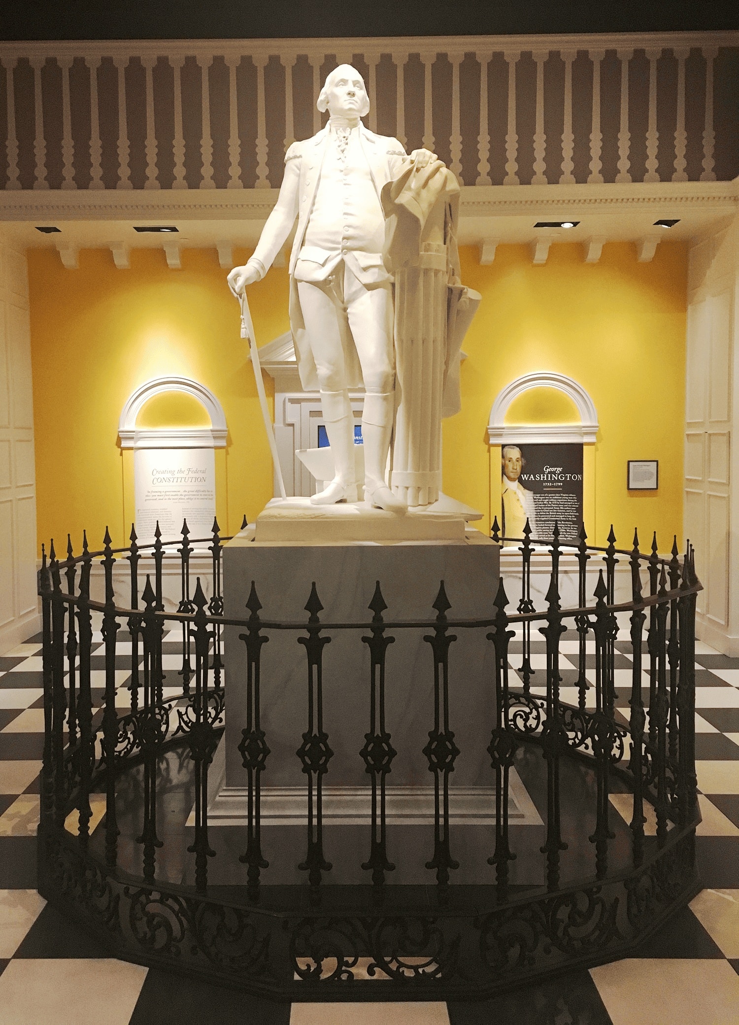 6-Day United States History Road Trip Itinerary Inspired by Hamilton the Musical 9 Exhibit of George Washington at the American Revolution Museum in Yorktown, displaying a life-size figure in Continental Army uniform beside historical text panels surrounded by a iron gate, an important stop on an American History Tour.
