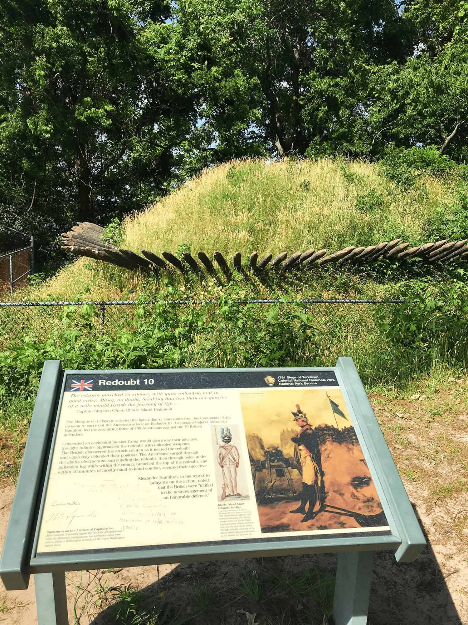 6-Day United States History Road Trip Itinerary Inspired by Hamilton the Musical 28 Redoubt 10 at Yorktown Battlefield, a grassy earthwork fortification with wooden defenses and historical signage mentioning Alexander Hamilton, marking a key site in the final assault of the American Revolutionary War.