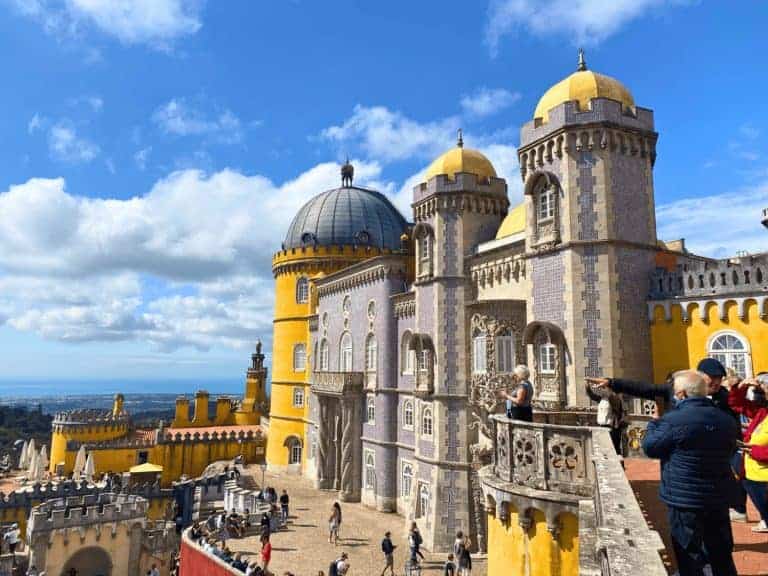 Colorful exterior of the National Palace of Pena with its red and yellow towers atop a lush hill, showcasing the whimsical architecture of Sintra Portugal.