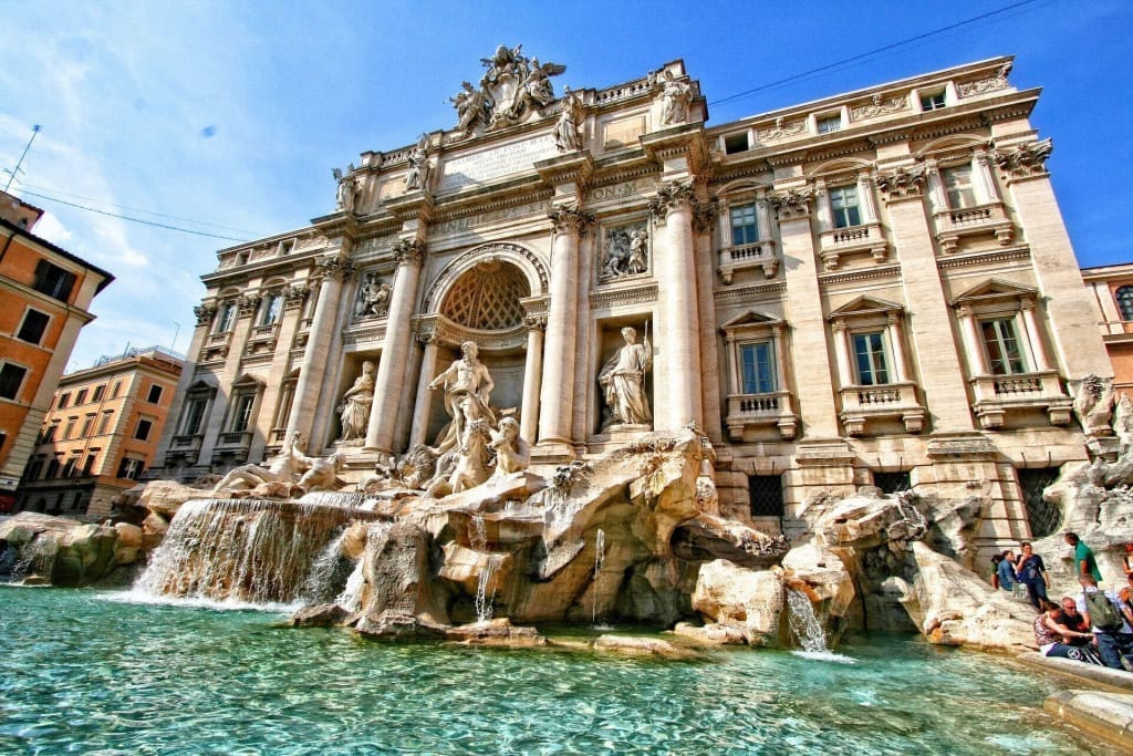 3-Day Rome, Italy Itinerary: A Day-to-Day Plan for First-Timer Visitors 3 Wide shot of the trevi Fountain in Rome, Italy, featuring cascading water and intricate Baroque sculptures of Oceanus and sea horses under a blue sky.