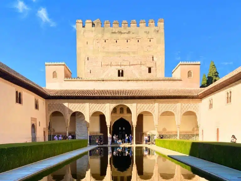 Is Granada, Spain, Worth Visiting? Yes, Here's How I Took a Day Trip 13 Court of the Myrtles within the Nasrid Palaces at the Alhambra complex in Granada, Spain, looking north towards the Comares Tower, featuring a long reflective pool lined with myrtle bushes and bordered by Moorish arches and intricate stucco walls. The courtyard exemplifies the symmetry and elegance of Islamic palace architecture.