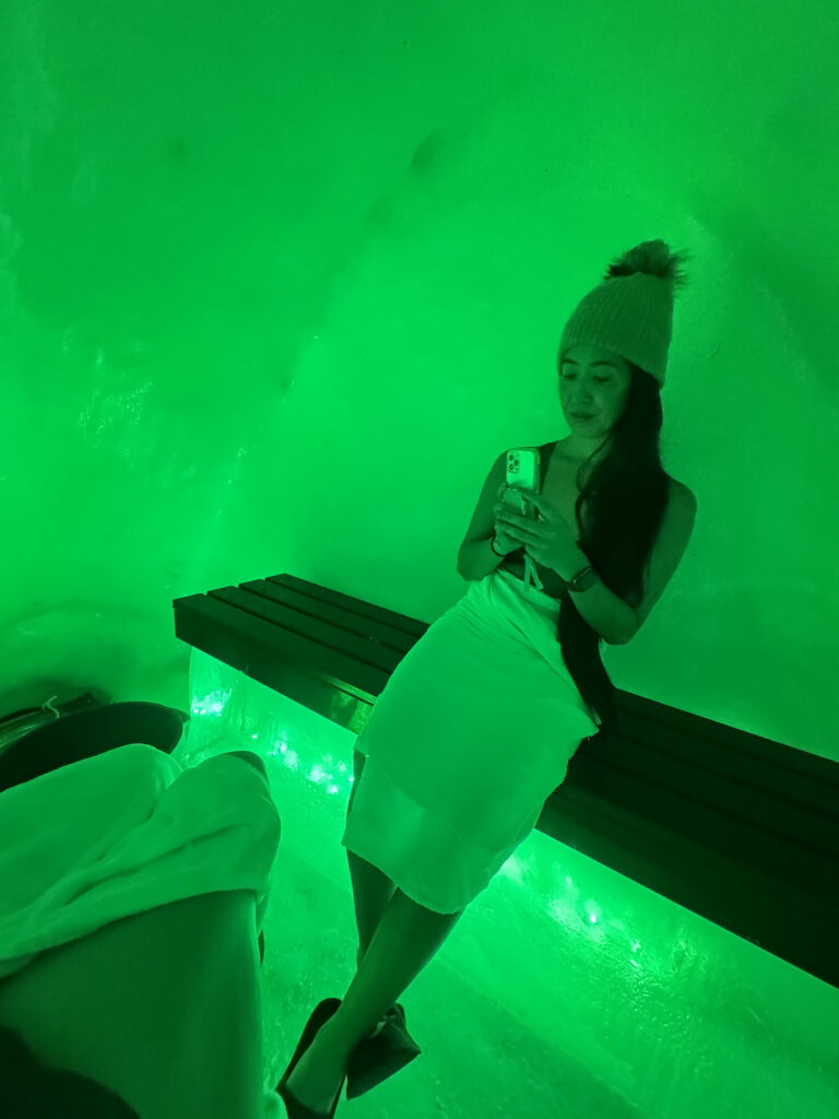 Is Rovaniemi, Finland, Worth Visiting? 19 Reasons You Should Visit in Winter 18 Woman in stylish bathing suit sitting on glowing bench in unique green-lit snow sauna at the Arctic Snow Hotel in Lapland Finland.