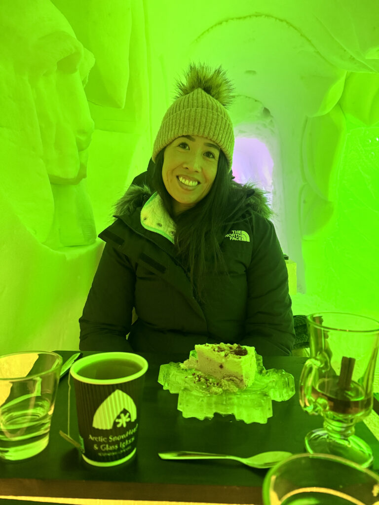 30 of the Best Things to Do in Rovaniemi, Finland, This Winter 50 Woman enjoying dessert inside illuminated ice structure with unique green lighting in Finland.