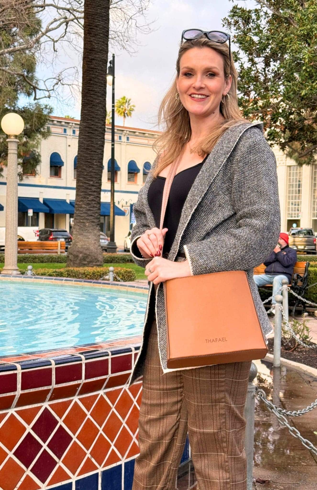 5-Day Austria Travel Itinerary: How to Visit Vienna and Salzburg on a Budget 84 Chic woman smiling by a colorful tiled fountain in a vibrant outdoor park while holding a Thafael vegan leather bag.