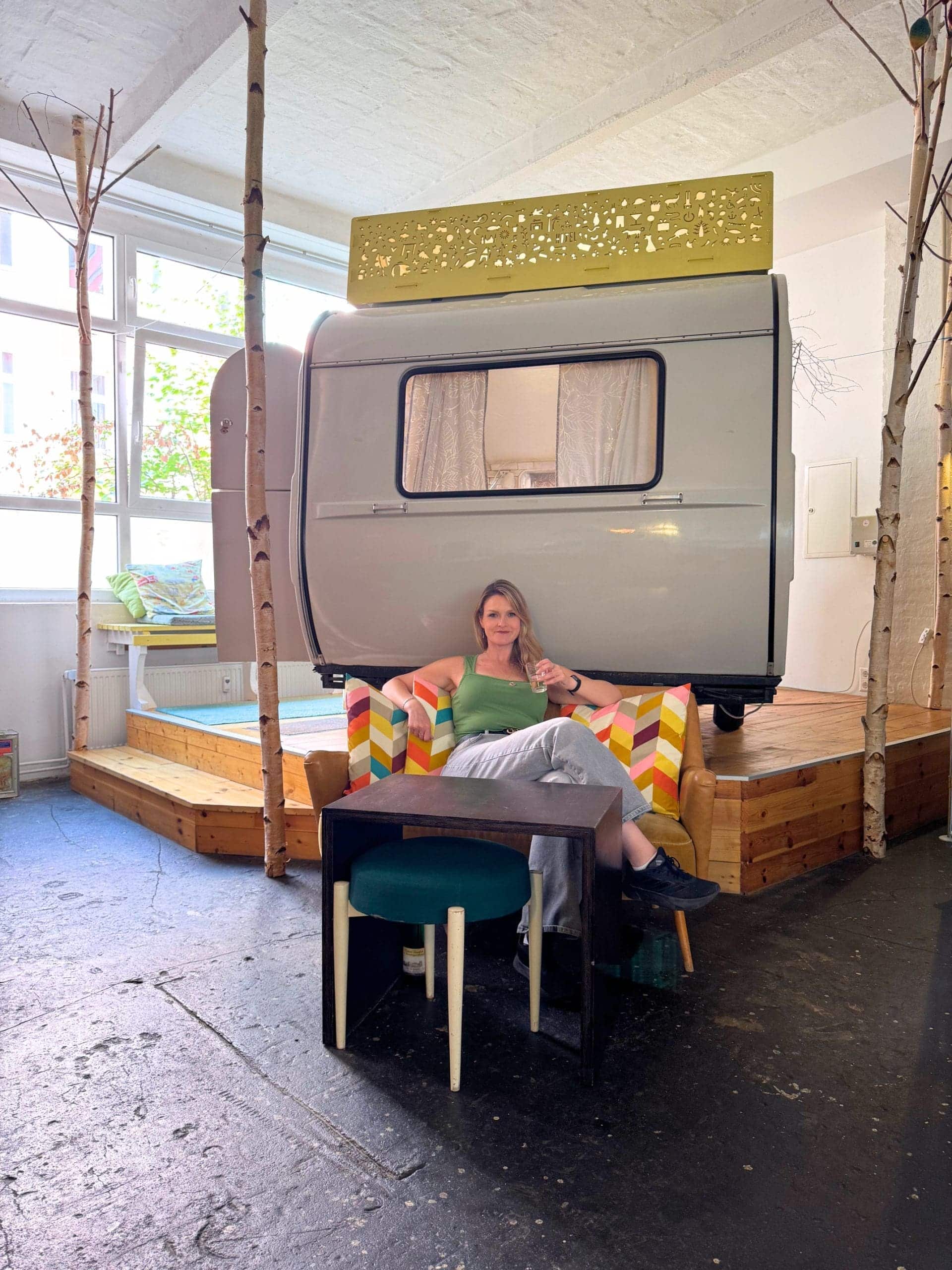 13 Pros & Cons of Solo Travel You Need to Know Before Booking—Female Traveler Advice 3 Cozy Hüttenpalast Berlin interior with Kleine Schwester caravan, vibrant couch, and a woman enjoying wine.
