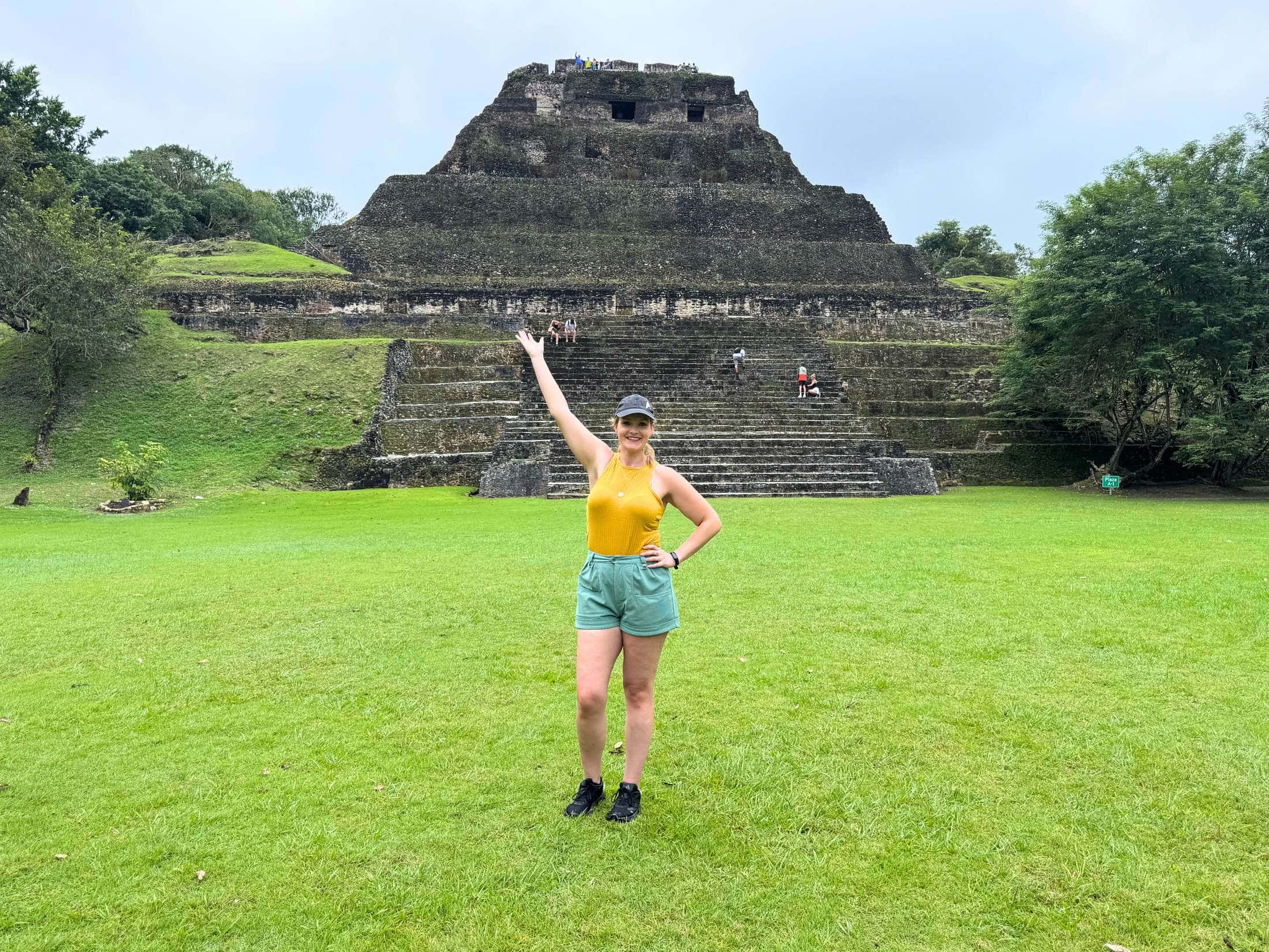 Resources 26 Michelle L. Jensen (Travel HerStory) standing at the base of El Castillo at Xunantunich, Cayo District, Belize, a towering Maya pyramid with intricate stone carvings near the summit. The ancient structure rises dramatically above the surrounding jungle landscape.