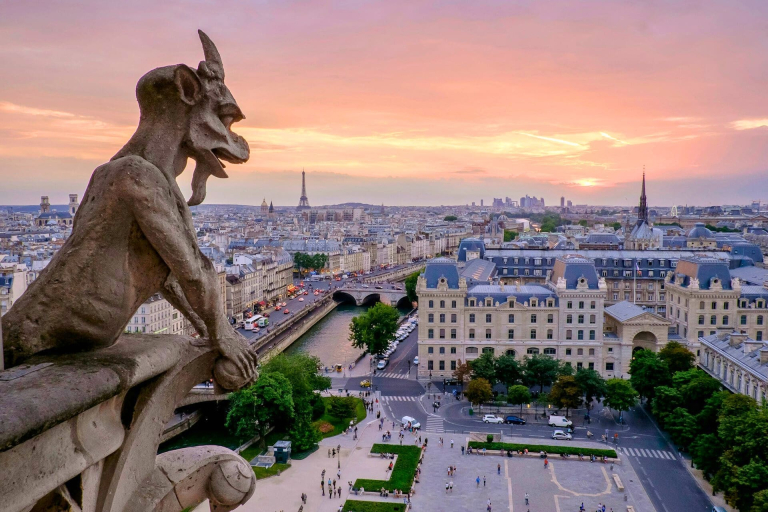 Beautiful sunset view of the Paris, France, skyline from the towers of the Notre Dame Cathedral, featuring one of its famous gargoyles in the foreground.