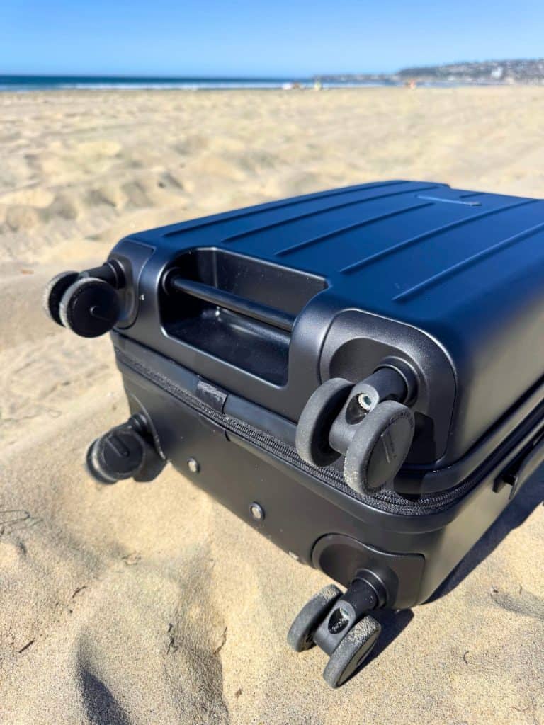 How to Choose a Vacuum-Seal Carry-On: Complete Guide for Space-Saving Travelers 7 Close-up of the BlackVoyage AirCabin Pro carry on suitcase handle and wheels, highlighting four smooth, 360-degree spinner wheels attached to the sleek, hard-shell bottom of the suitcase laid on sand on a sunny day.