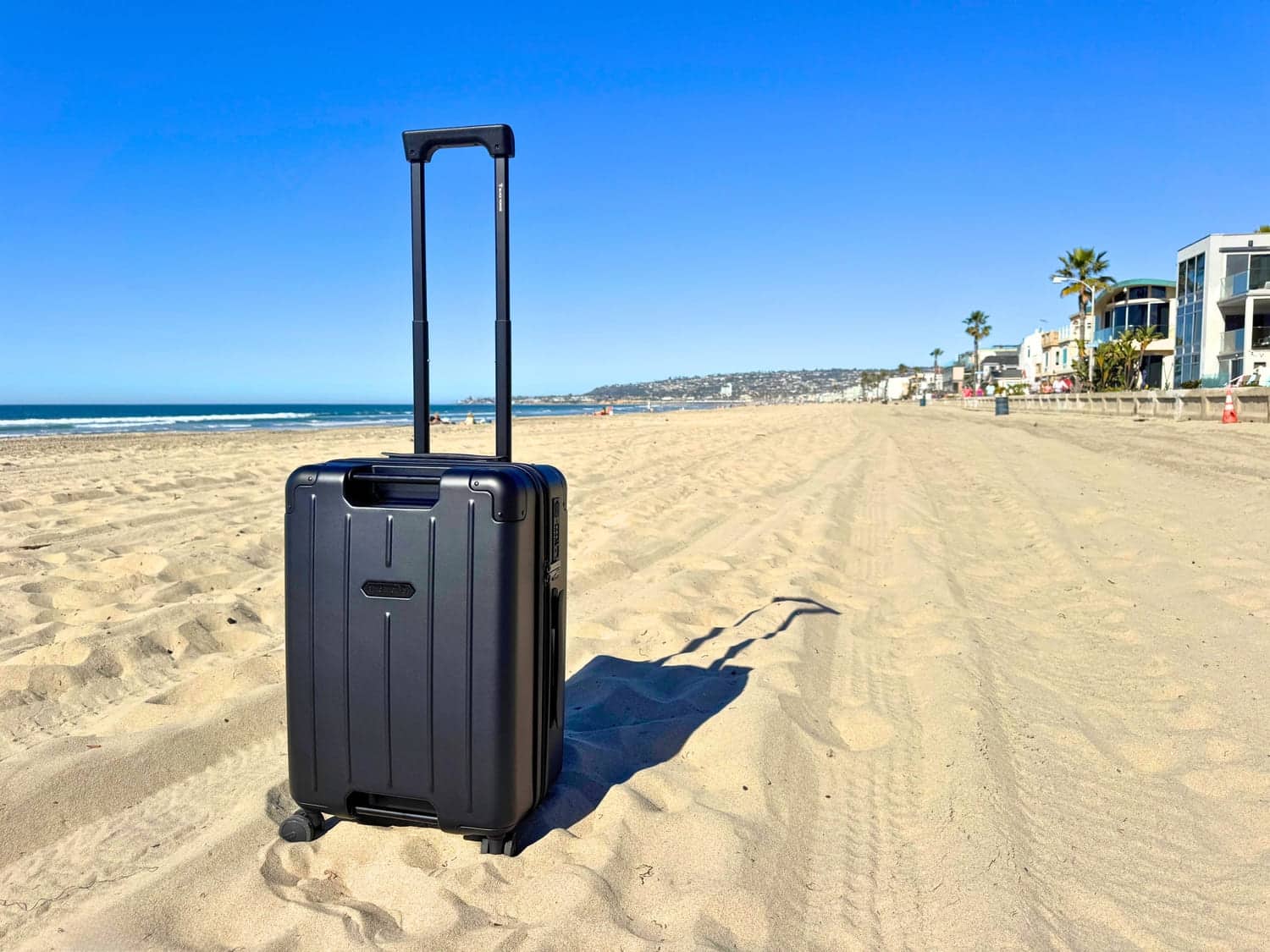 The BlackVoyage AirCabin Pro black carry on suitcase on a sandy beach with it's handle extended under a clear sky.