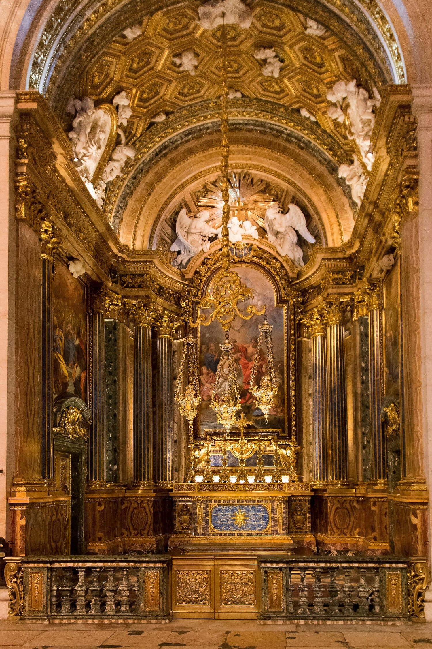 22 of the Best Things to Do in Lisbon, Portugal (My Budget-Friendly Picks) 14 Ornate gilded altar of the Chapel of São João Baptista inside Igreja de São Roque, Lisbon, Portugal. Lavish Baroque interior features gold-covered columns, white marble angel sculptures, a central religious painting, hanging chandeliers, and a richly decorated coffered arch above the altar.